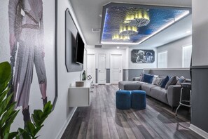 Ett modernt vardagsrum med en grå soffa, blå sittpallar och en platt-TV som är monterad på väggen.