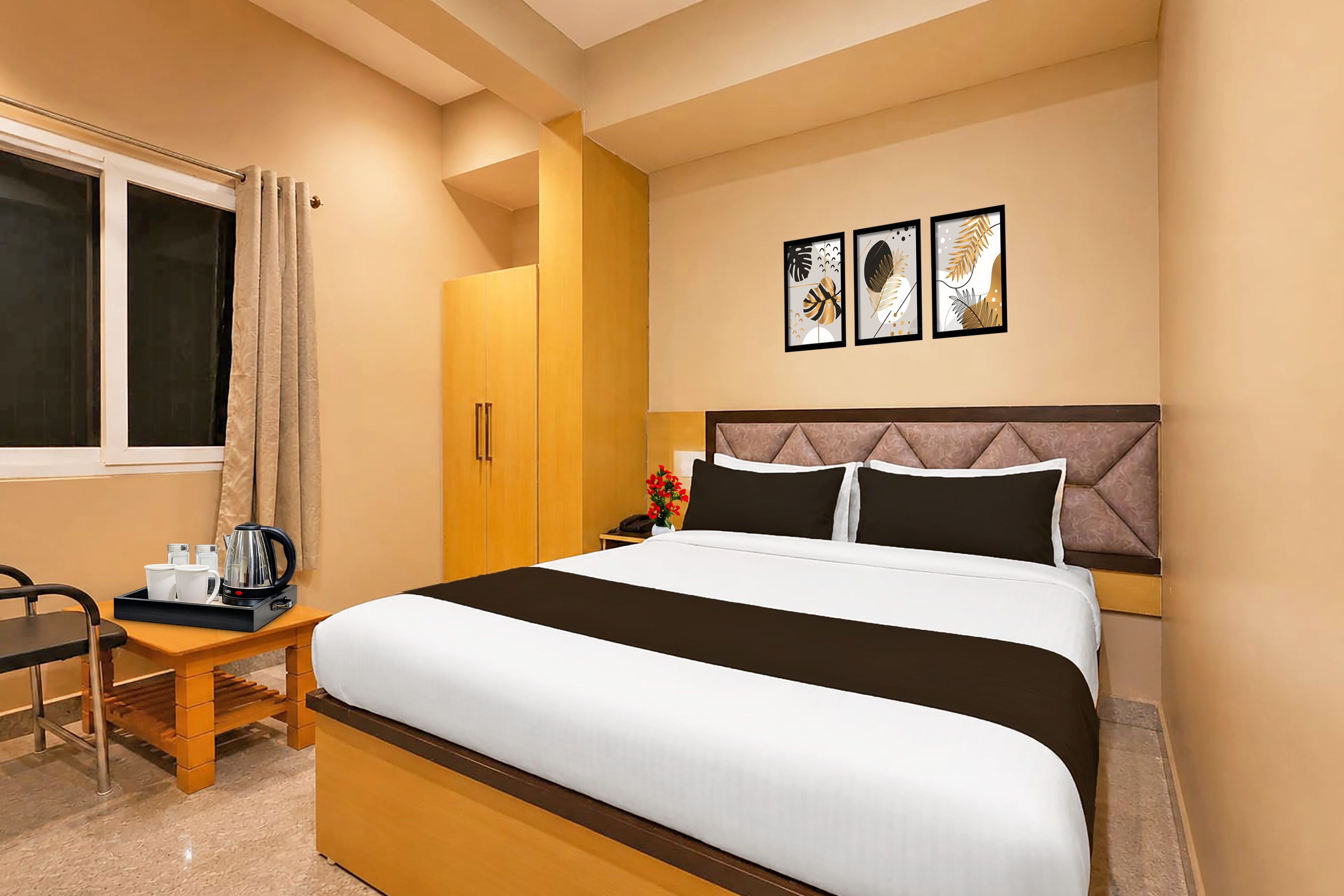 A hotel room with a bed, a desk with a kettle, a wardrobe, and three framed pictures on the wall.