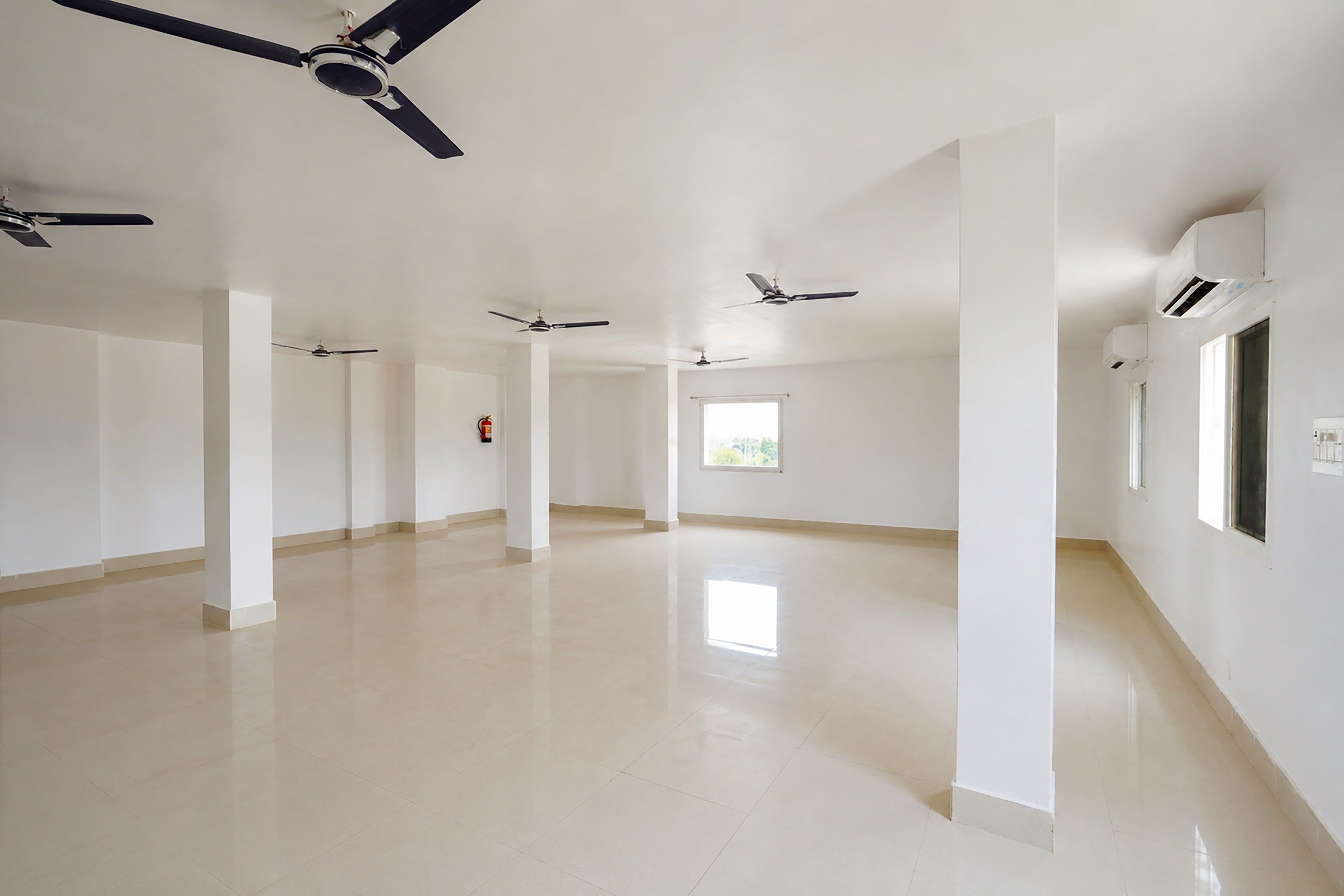 A spacious, empty hotel corridor with multiple ceiling fans, white walls, and a tiled floor.