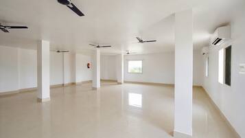 A spacious, empty hotel corridor with multiple ceiling fans, white walls, and a tiled floor.