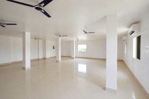 A spacious, empty hotel corridor with multiple ceiling fans, white walls, and a tiled floor.