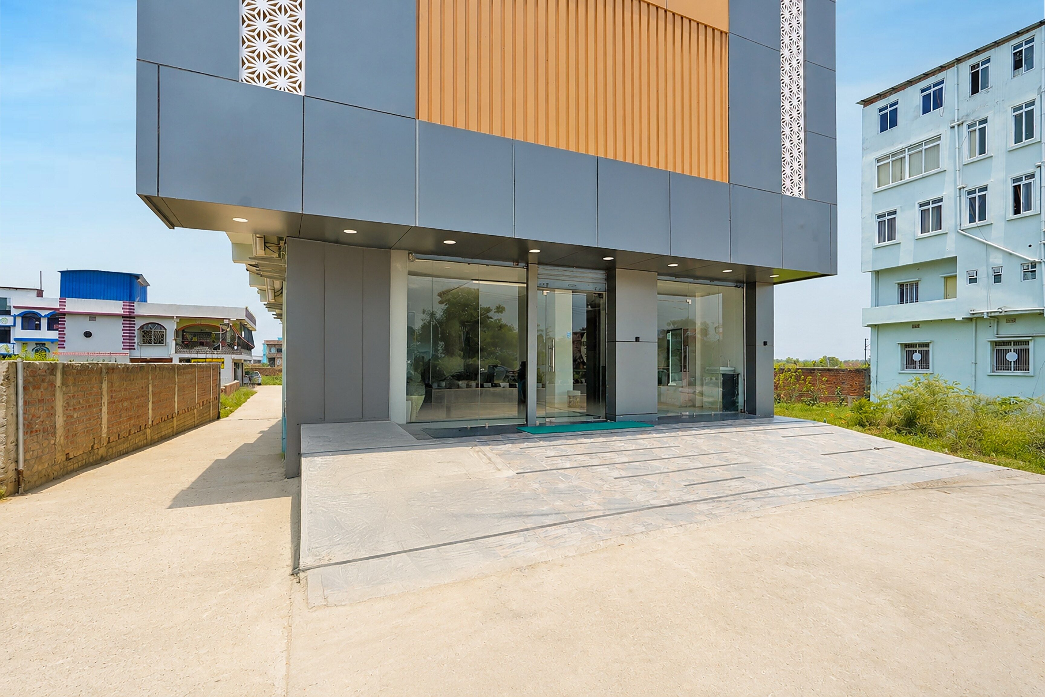 A modern building with a glass entrance, a concrete ground floor, and a mix of grey and wooden paneling on the upper floors.