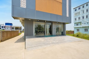 A modern building with a glass entrance, a concrete ground floor, and a mix of grey and wooden paneling on the upper floors.