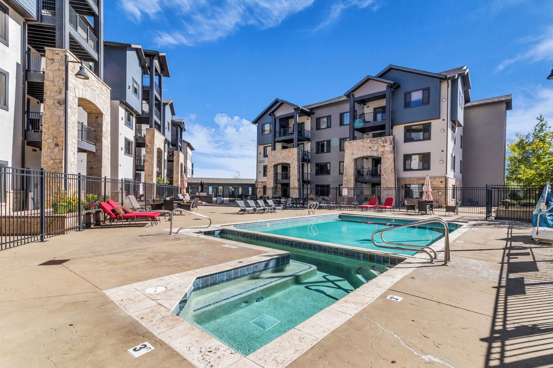 A multi-story residential building with a swimming pool, outdoor seating, and a stone facade.