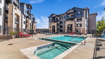 A multi-story residential building with a swimming pool, outdoor seating, and a stone facade.