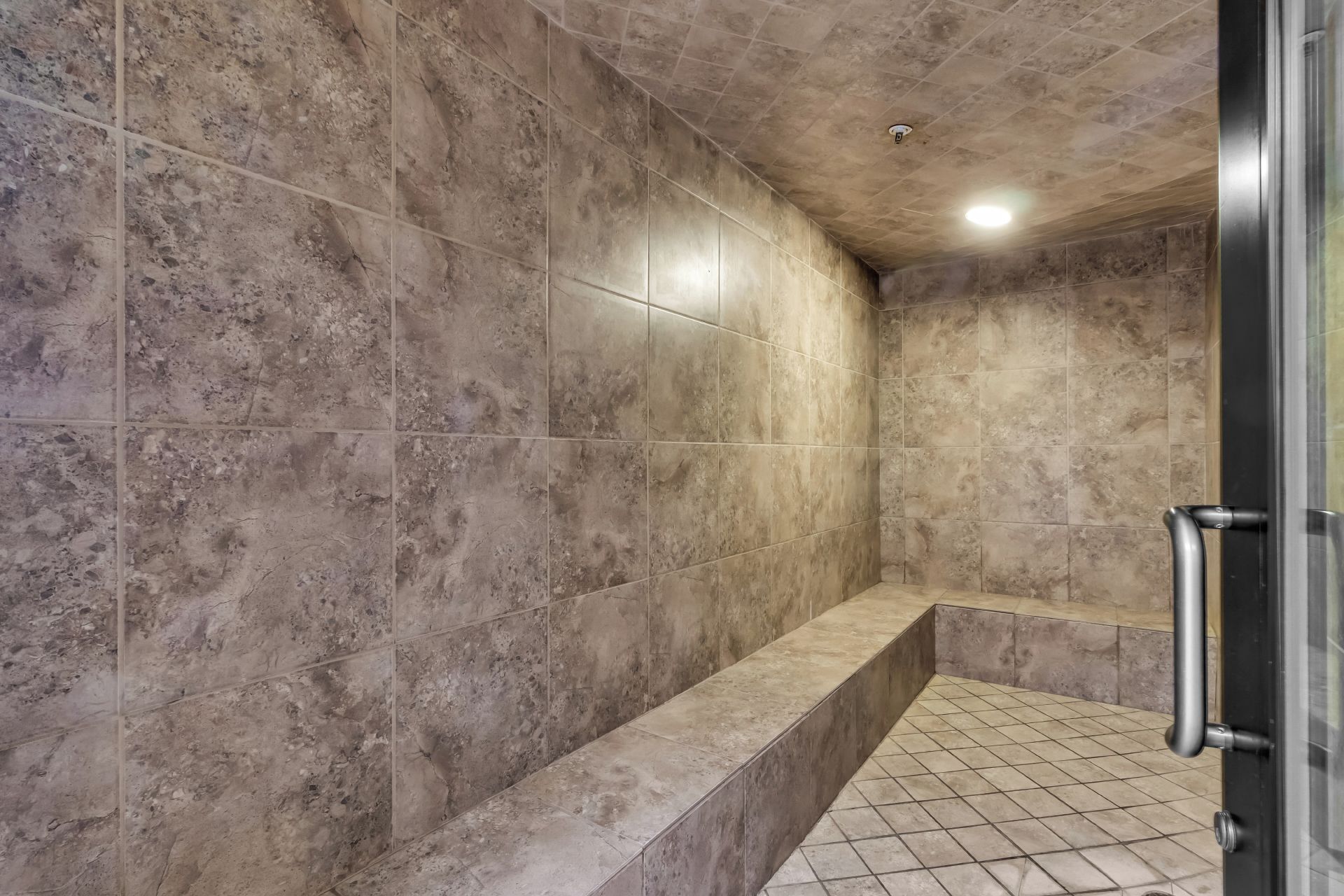 Une salle de bain avec une douche carrelée, un banc et une porte en verre.