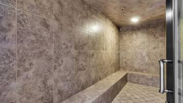 Une salle de bain avec une douche carrelée, un banc et une porte en verre.