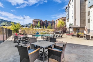 An outdoor patio with tables and chairs, a pool, and a view of multi-story buildings in the background. - Silverado Lodge by All Seasons Resort Lodging (Park City)