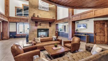 Un hall d’entrée spacieux avec une cheminée en pierre, des fauteuils en cuir et un plafond en bois.