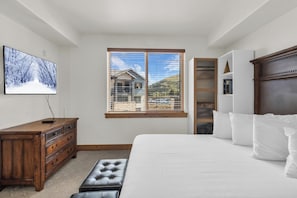 A bedroom with a large bed, a dresser, a television, and a window with blinds. - Silverado Lodge by All Seasons Resort Lodging (Park City)