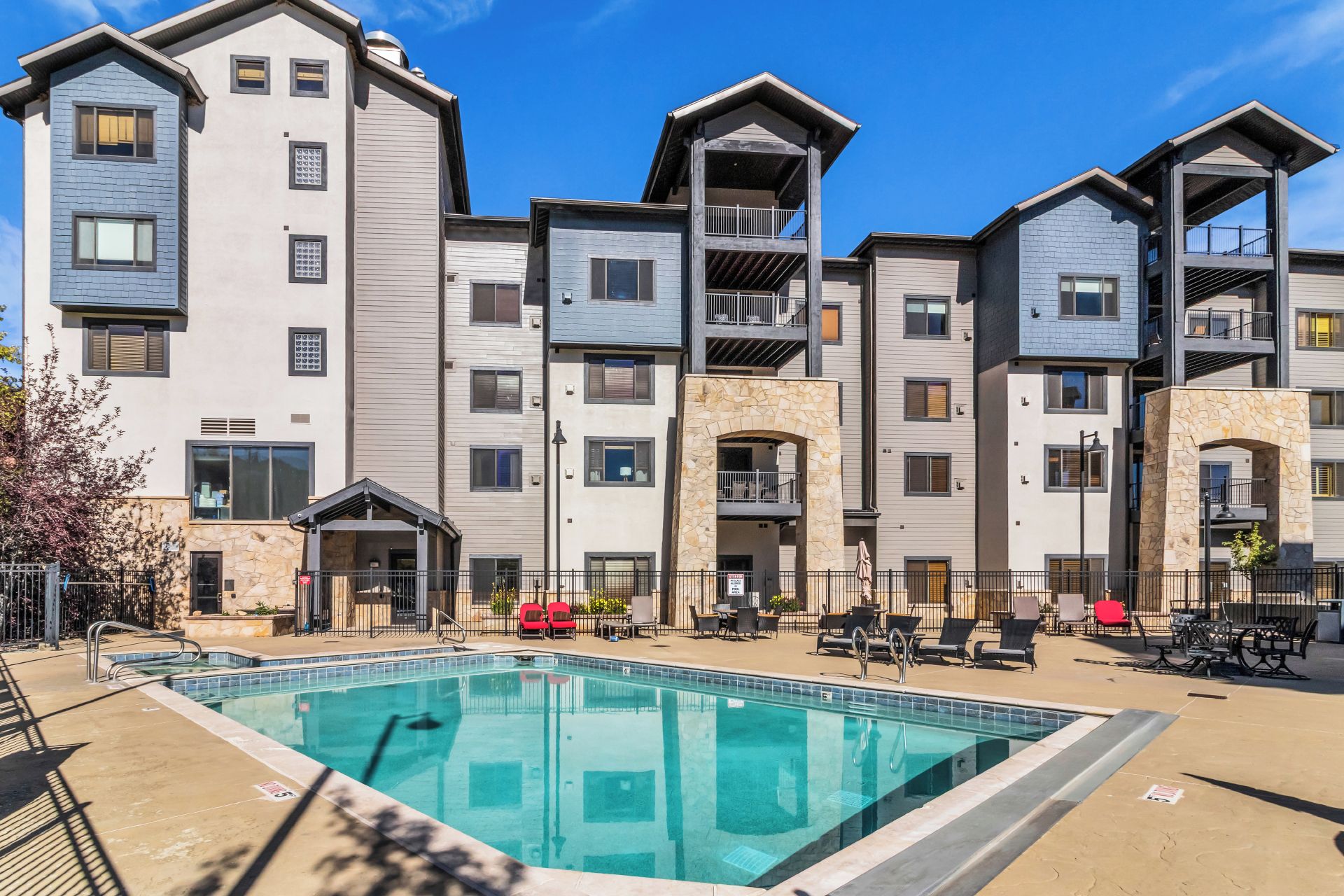 A modern apartment building with a swimming pool, outdoor seating, and balconies.