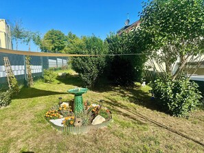 A garden with a birdbath, flowers, and a ladder leaning against a wall.