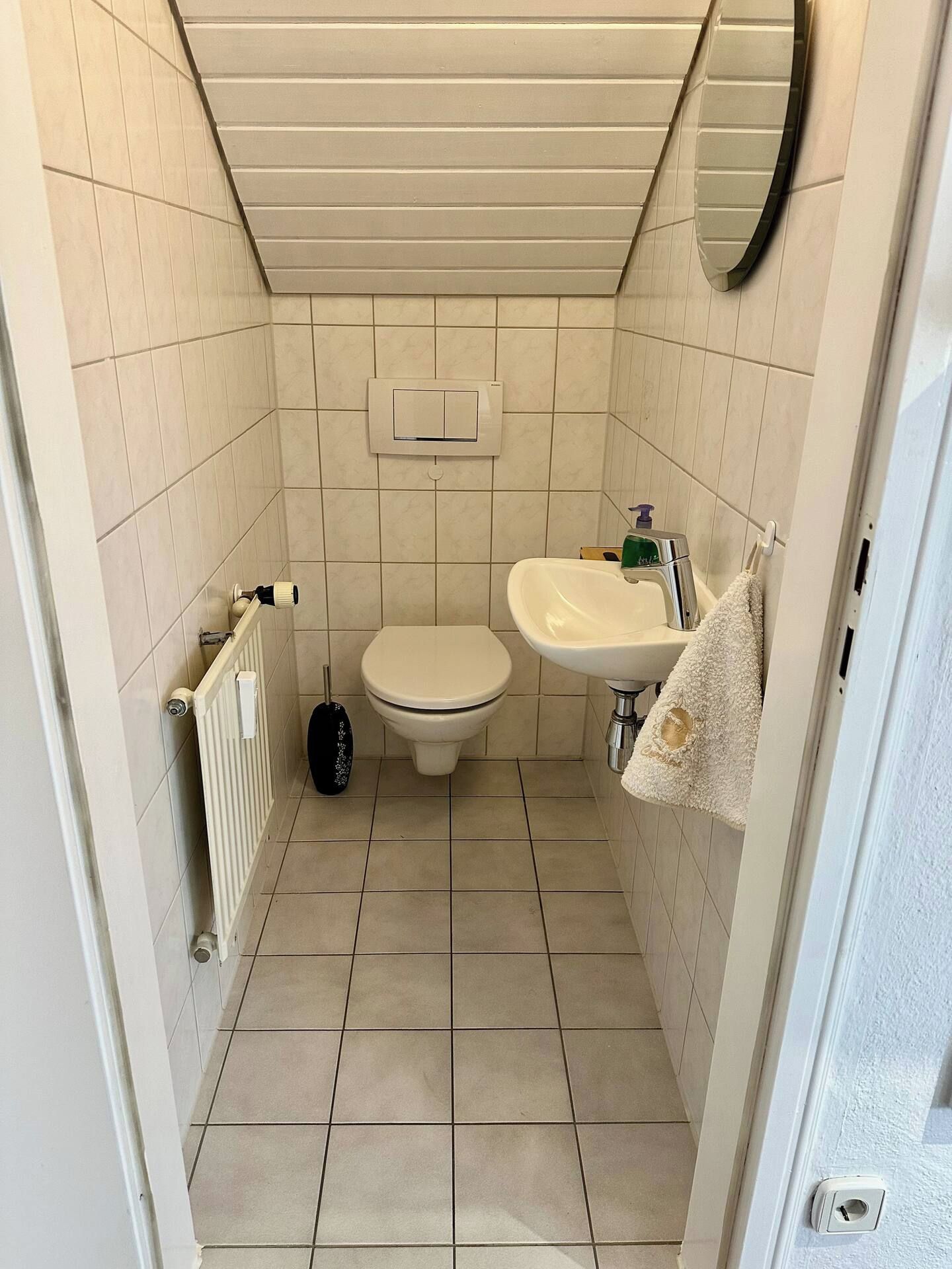 Ein kleines Badezimmer mit Fliesen, Toilette, Waschbecken und Heizkörper.