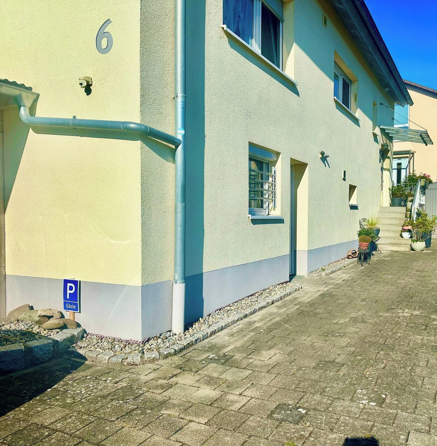 En bygning med nummer '6' på muren, et blåt parkeringsskilt og en asfalteret vej.