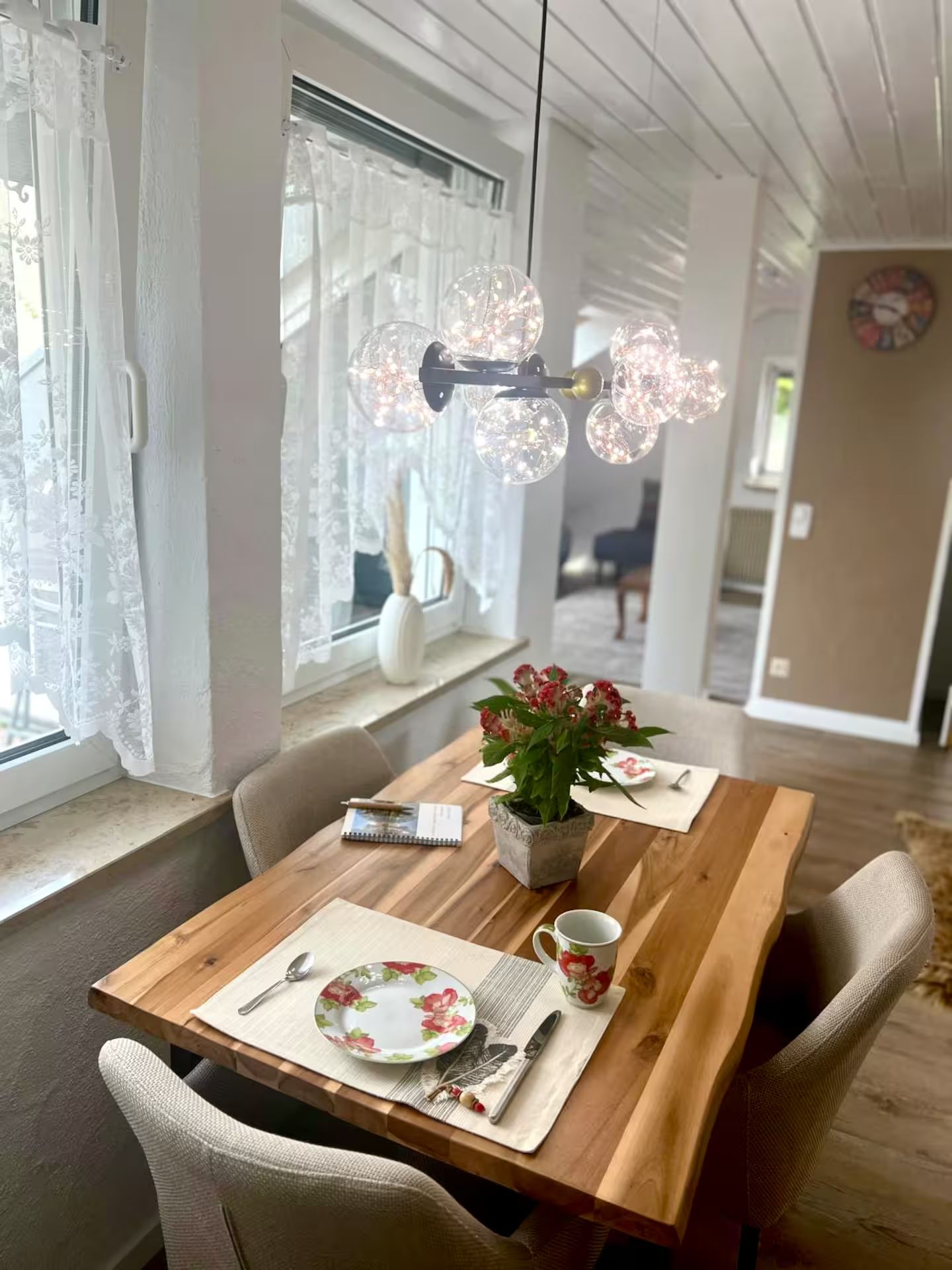 Ein Essbereich mit einem Holztisch, Stühlen, einer Blumenvase und einer Hängelampe.