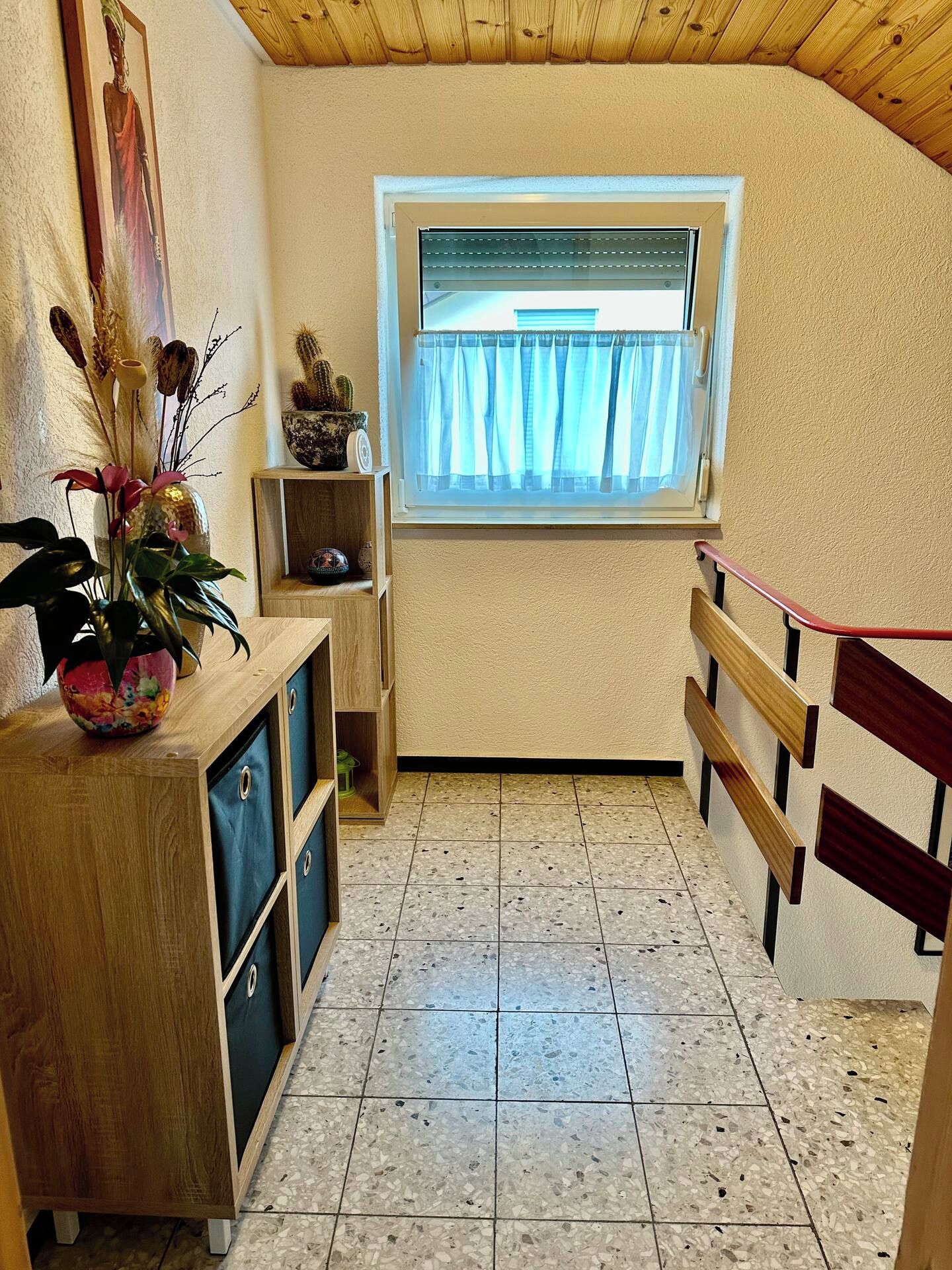 Ein kleiner Raum mit Fenster, einem Holzschrank und einem Fliesenboden.