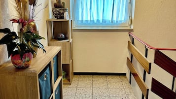 Ein kleiner Raum mit Fenster, einem Holzschrank und einem Fliesenboden.