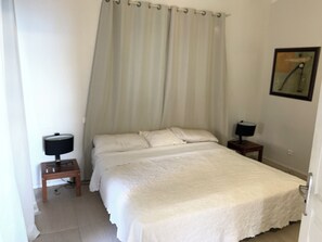 A bedroom with a double bed, a bedside table with a lamp, a small wooden stool, and a curtain. - New Listing (SAINT MARTIN)