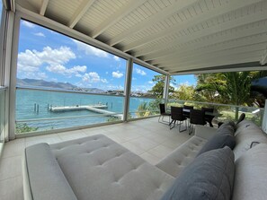 Ein modernes Wohnzimmer mit einem großen Panoramafenster mit Blick auf ein Gewässer, einen Pool und eine ferne Bergkette.