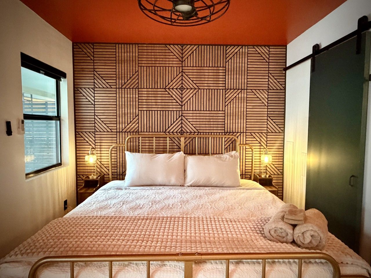 Un lit bien fait, avec une couvre-lit à motifs, deux oreillers et un ensemble de serviettes posé sur une table de chevet.