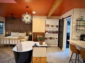 Una camera da letto moderna con un letto, un comodino e una scrivania. C'è un bagno con una vasca e un water. La stanza ha un soffitto in legno e un muro decorato.