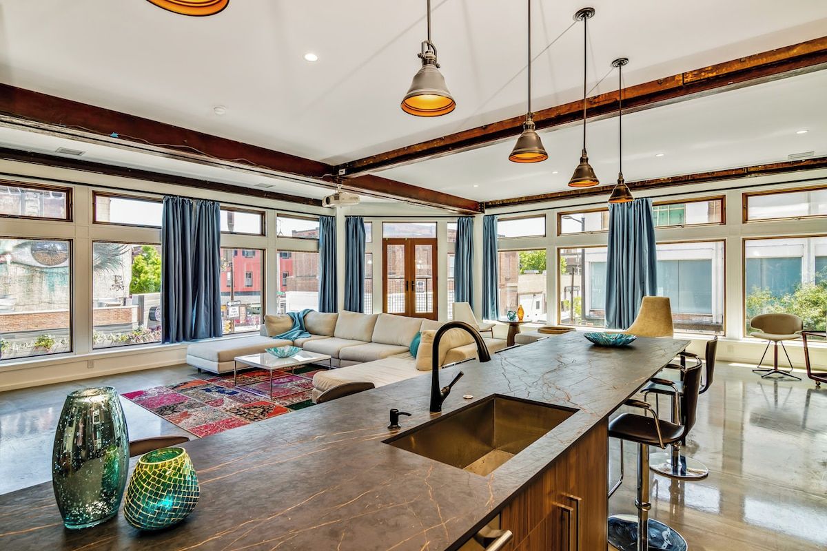 A spacious kitchen with a central island, large windows, and modern pendant lighting.