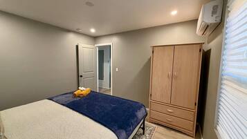 A bedroom with a bed, a wardrobe, a door, and an air conditioning unit.