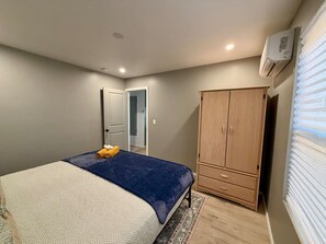 A bedroom with a bed, a wardrobe, a door, and an air conditioning unit.