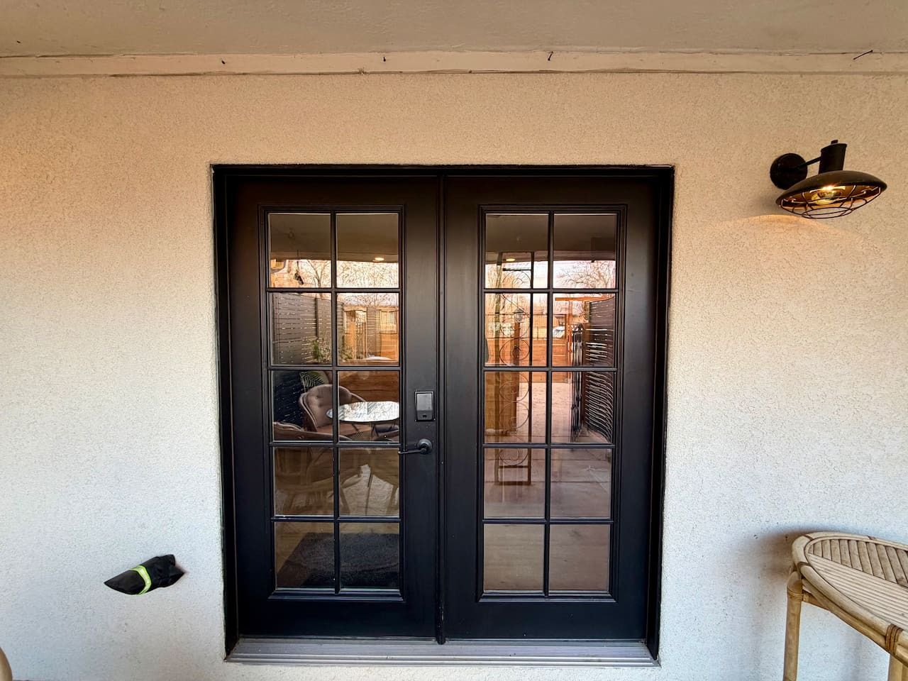 A black-framed glass door with a small step leading up to it, a wall-mounted light fixture to the right, and a chair to the right of the door.