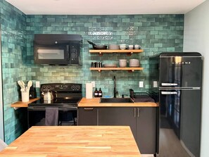 A kitchen with a microwave, stove, refrigerator, and shelves with dishes.