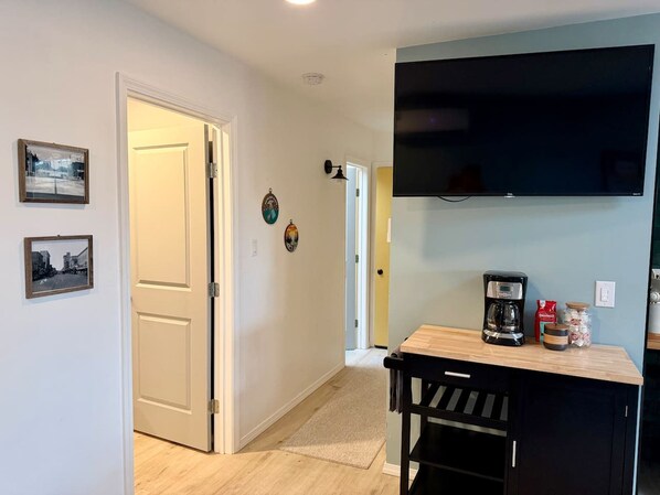 A hallway with a door, a coffee maker, and a TV on the wall.