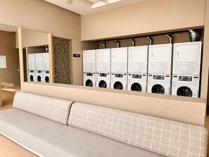 A laundry room with multiple washing machines and dryers, a bench, and a mirrored wall. - Reserva Apartment – Bello Horizonte by SOHO – 392A (Santa Marta)