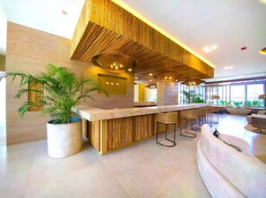 A modern reception area with a wooden reception desk, bar stools, and a large potted plant. - Reserva Apartment – Bello Horizonte by SOHO – 392A (Santa Marta)