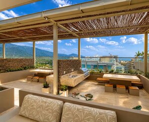 Eine Dachterrasse mit Steinmauern, einem Grill und Sitzbereichen mit Kissen.