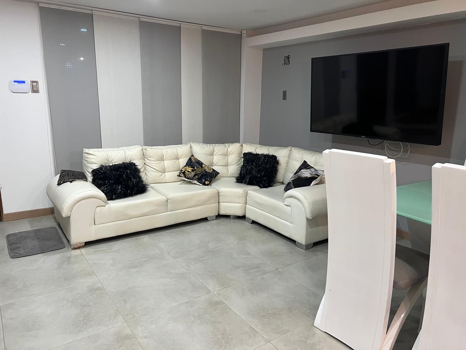 A modern living room with a sectional sofa, a flat-screen TV, and a glass coffee table.