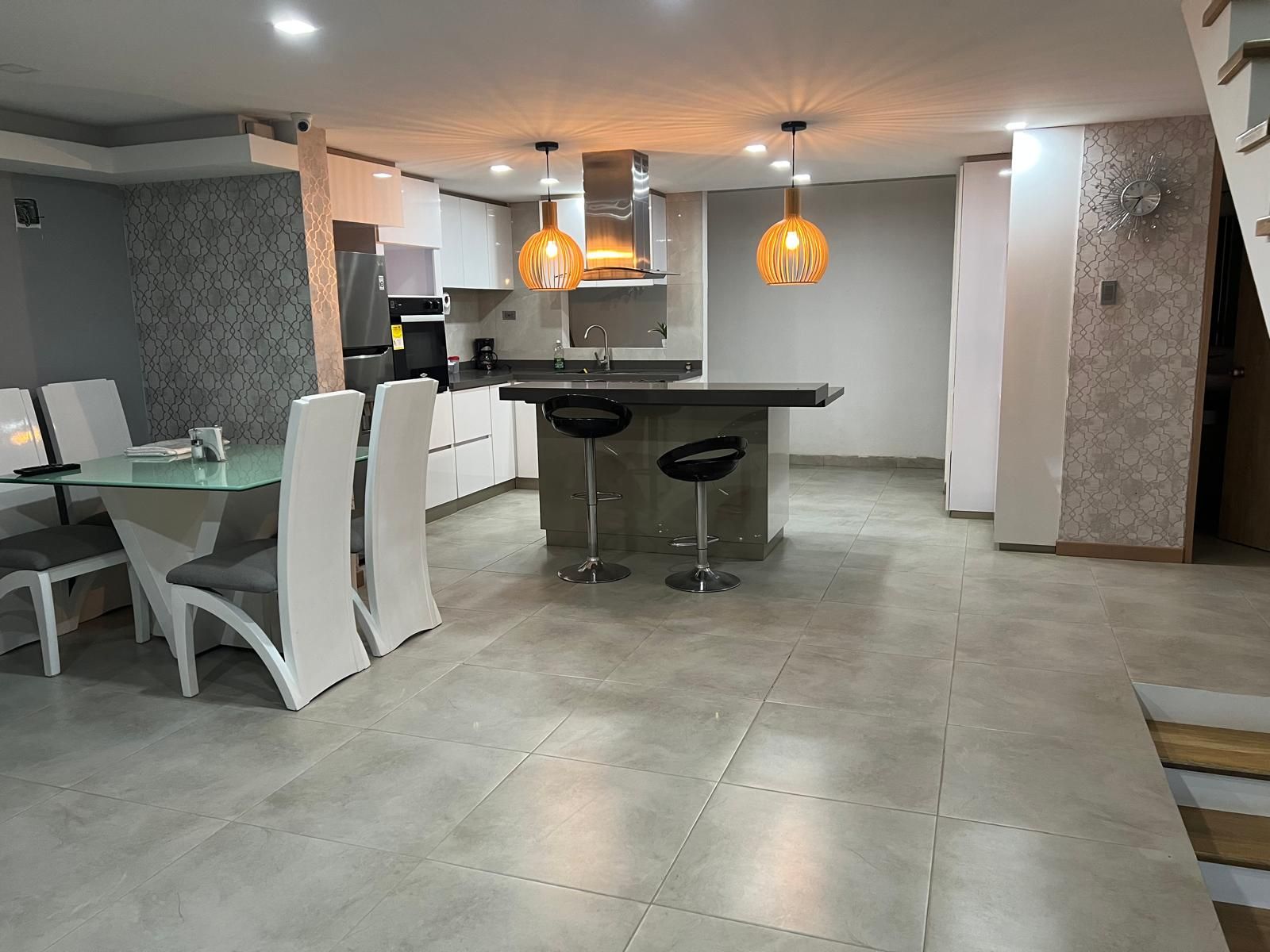A modern kitchen with a central island, bar stools, and pendant lighting.