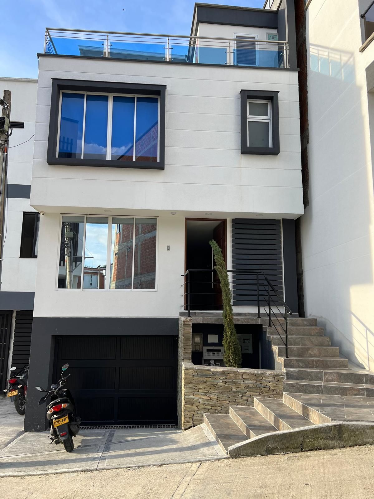 Ett modernt hus i två våningar med ett garage, en trappa och en motorcykel parkerad framför.