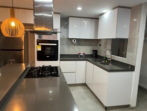 Une cuisine moderne dotée d’appareils électroménagers en acier inoxydable, d’un four encastré, d’une cuisinière à gaz et de meubles de rangement blancs.