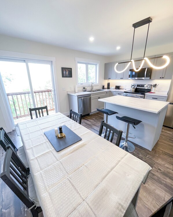 A modern kitchen with a central island, stainless steel appliances, and a dining area with a white table and chairs.