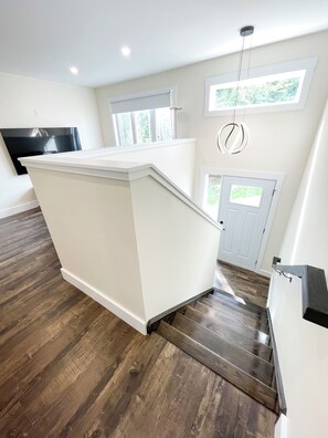 A modern kitchen with a white island, wooden flooring, and a view of the outdoors through windows.
