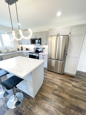 A modern kitchen with a central island, stainless steel appliances, and a wooden floor.