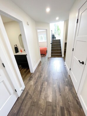 A hallway with wooden flooring, white walls, and a staircase leading to an upper level.
