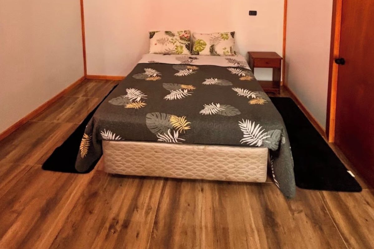 A small, compact bedroom with a bed, a nightstand, and a door.