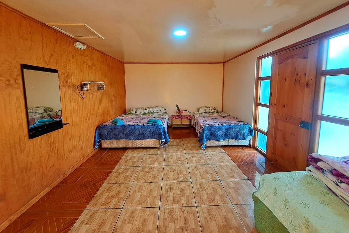 A room with two beds, a wooden floor, a mirror, and a door leading outside.