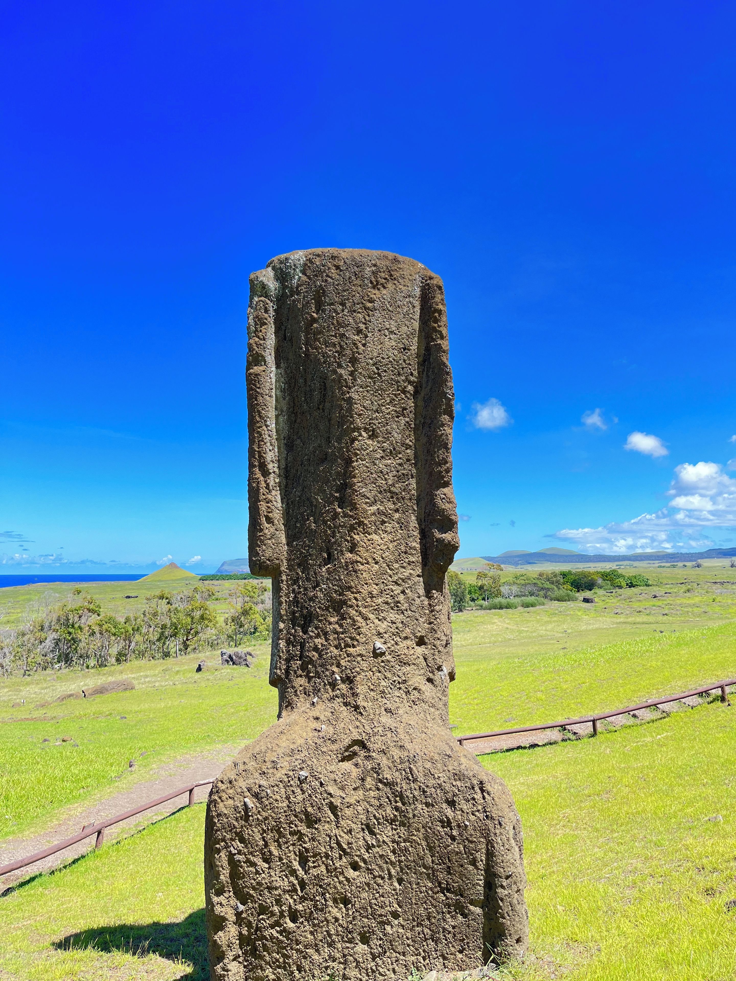 A tall, narrow stone structure with a flat top, surrounded by a grassy field and a clear blue sky.
