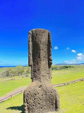 A tall, narrow stone structure with a flat top, surrounded by a grassy field and a clear blue sky. - Hare Tupuna O Piri Nui (Hanga Roa)