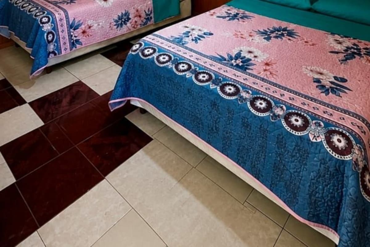 A room with two beds, wooden walls, a tiled floor, and a ceiling fan.