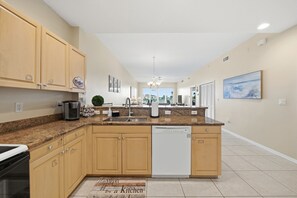 A modern kitchen with granite countertops, wooden cabinets, a dishwasher, and a central island. - Spacious 3-bedroom family-friendly condo in Clearwater Beach (Clearwater)
