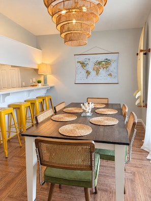 A dining area with a wooden table, yellow bar stools, wicker chairs, and a world map on the wall. - Endless Summer Surf Shack 4 min to beach Walk to Restaurants (Panama City Beach)