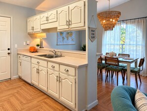 A kitchen with white cabinets, a double sink, and a dining area with a table and chairs. - Endless Summer Surf Shack 4 min to beach Walk to Restaurants (Panama City Beach)